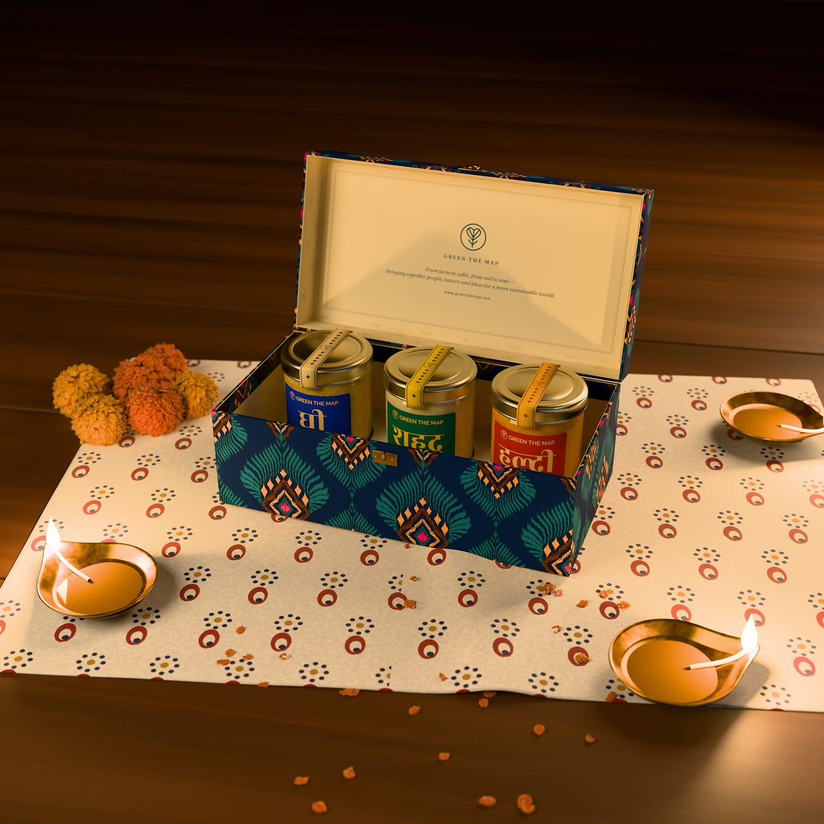 The open 3-jar gift box on a block-printed cloth with lit brass diyas and marigolds.