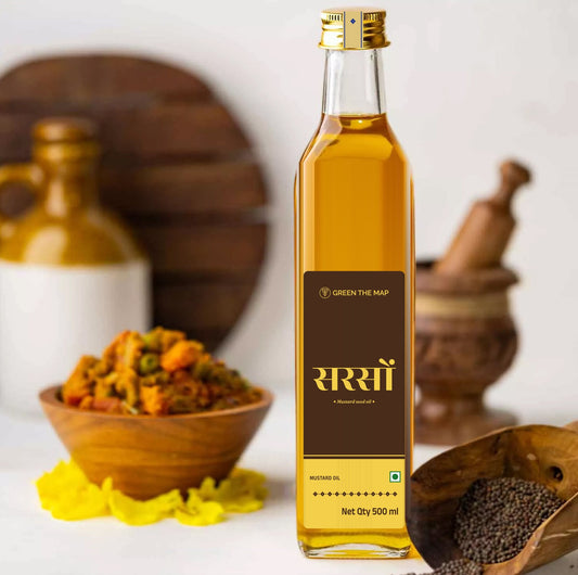 Mustard oil 500 ml in a square glass bottle with its dark brown Sarson label, beside a bowl of pickle, a mortar and mustard seeds.