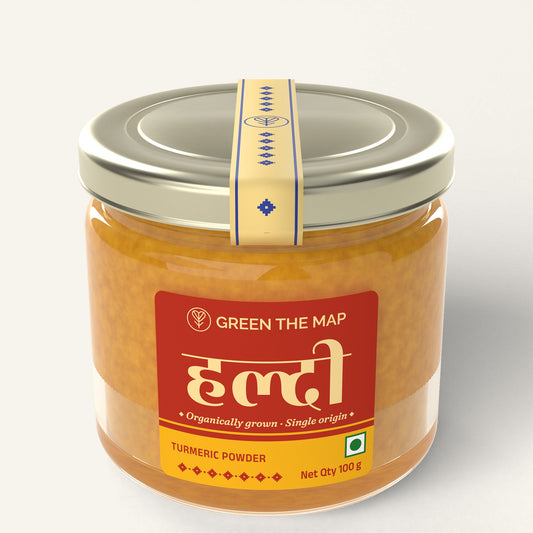 Turmeric powder 100 g in a glass jar with a red label and a champagne gold cap, on a plain off-white background.
